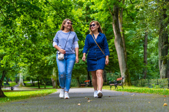 Two young beautiful smiling women dressed casual walking in city park on sunny day, trees in background. Meeting of friends. Walk in park.
- Powered by Adobe