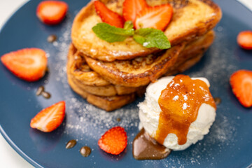 French toast garnished with strawberries and mint, with ice cream and caramel sauce on a blue plate. Delicious and healthy breakfast. Close-up