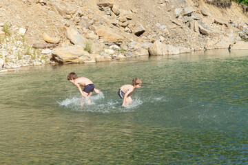 Happy boys are playing in the mountain river. They splash on each other