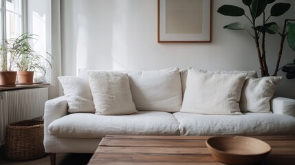 A modern living room with a white sofa, multiple cushions, a wooden table, several potted plants, and large windows letting in abundant natural light, creating a cozy atmosphere.