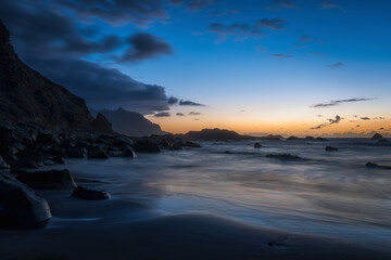 Fototapeta premium Tenerife, June 2022: A rock strewn bay at sunset with the tide rolling in