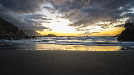 Obraz premium Tenerife, June 2022: A rock strewn bay at sunset with the tide rolling in