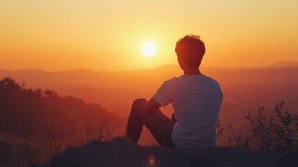 Obraz premium Asian man enjoying a quiet moment of reflection while watching the sunset from a hilltop, feeling inspired.