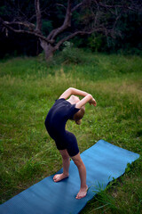 little 5-year-old girl in a black minimalist overall does gymnastics in the garden, outdoors