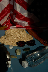 straw hat, sunglasses, bottle of water, sunscreen spray, american flag on colored background