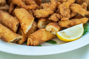 Chicken Fingers, Nuggets, and Ham-Cheese Dumplings: Fried Delights with Lemon and Lettuce, Served on White Plate.