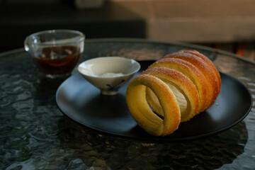 Kurtoskalacs, hungarian sweet chimney cake on a black plate. Served as a breakfast alongside black coffee, in a cafe environment
