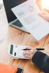 Close-up of hands using a calculator and reviewing financial documents at a wooden desk with a...