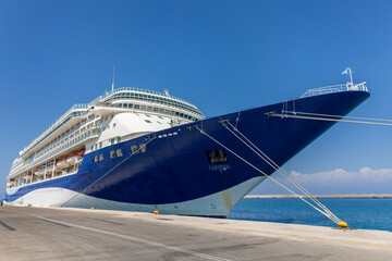 A big luxury cruise ship awaits passengers at the port in front of a clear blue sky in a sunny day.