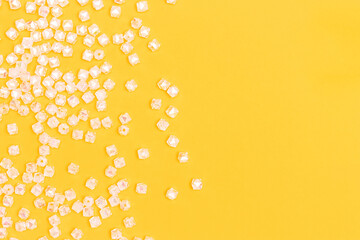 Transparent acrylic beads scattered on a yellow background with place for text.