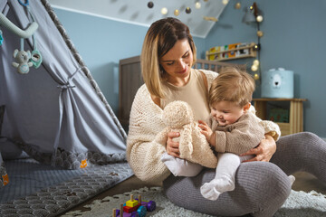 Mom plays with her little child in a kid room with toys and stuffed animals, a childrens wigwam tent in the background © leszekglasner