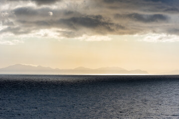 A breathtaking morning seascape from a merchant ship near Cape of Good Hope. The African coastline is faintly visible through the mist, as golden rays of the rising sun pierce ominous clouds.