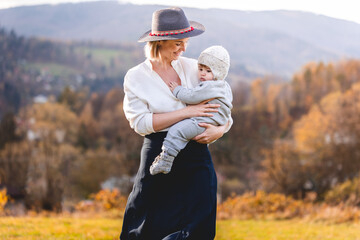 Mom tenderly hugs her little son during an autumn walk among the trees, they are wearing warm clothes