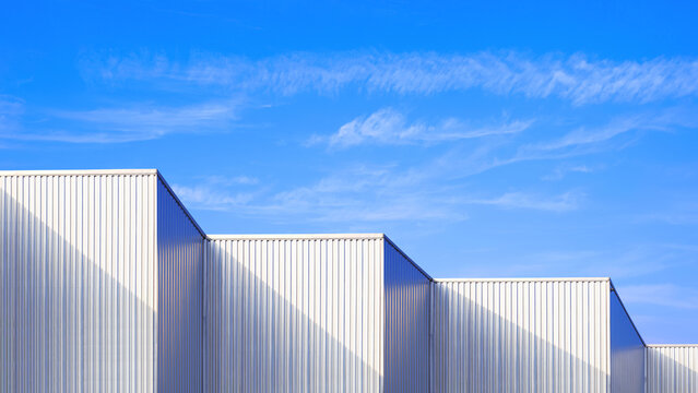 Fototapeta Factory industrial building with geometric metal corrugated steel wall and rooftop against blue sky background, Modern industrial exterior architecture backdrop design in minimal style