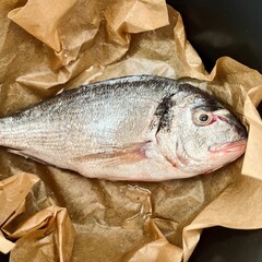 on brown parchment paper lies a whole raw Dorado fish cleaned of entrails in a black multicooker bowl. top view. dinner