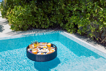 A floating breakfast tray with various dishes and drinks is located in the luxurious pool. The blue water sparkles in the sun. A place of rest and enjoyment.