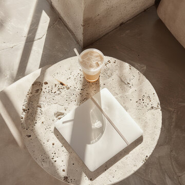 A MacBook rests on light grey concrete table, accompanied by refreshing iced coffee. sunlight casts soft shadows, creating serene and inviting atmosphere