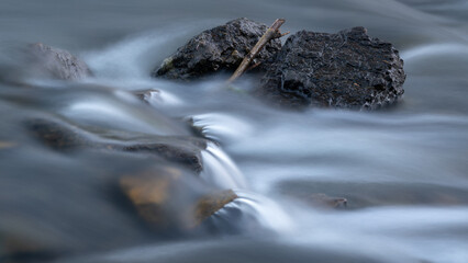 Rocks and wood in creek with silky water, long exposure