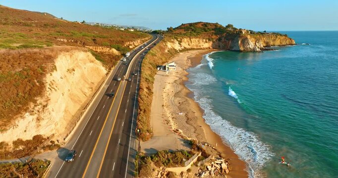 Four-lane highway with cars near the sandy beach along the coastline of the Pacific Ocean. Beautiful shore of Los Angeles, California, USA from top view.