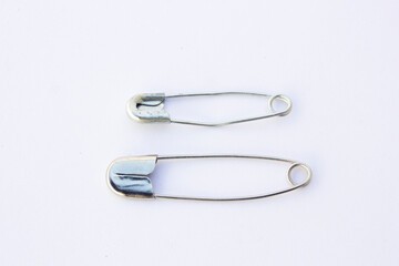 A close-up view of two metal safety pins—one larger and open, the other smaller and...