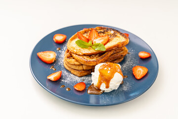 French toast garnished with strawberries and mint, with ice cream drizzled with caramel sauce, on a blue plate and orange juice on a white plate. Place for text.
