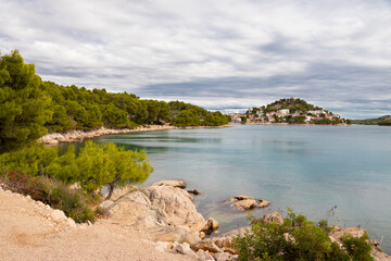 Rocky beach with hiking trail and hill with St Nicholas church in Tribunj, Croatia