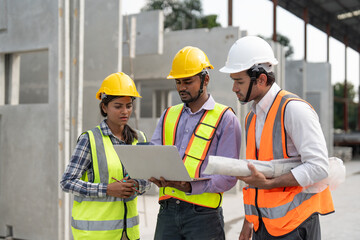 Team of construction engineers wearing vest and helmet safety discussing project at construction site. Group Indian foreman with laptop, paperwork working at factory making precast concrete wall.