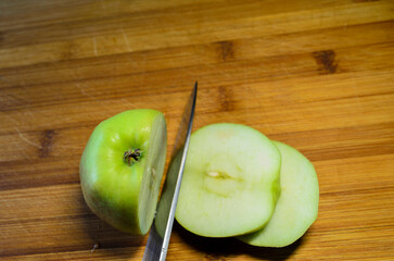 Apples being cut on a wooden chopping board with a kitchen knife