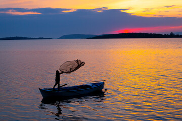 A fisherman throwing a net to fish in the lake