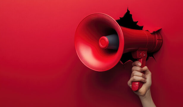 Hand holding megaphone breaking through red wall making announcement