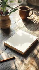 Blank notepad on a wooden table, with a cup and plant nearby.