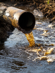 An iron pipe sticks out of the river and pollutes the water, the concept of environmental pollution, environmental disaster..