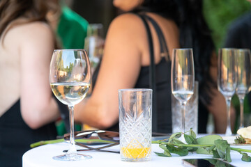 Close-up view of dirty drinking glasses with alcohol beverage wastes standing on white table on party or holiday celebration. Blurred women in the background. Soft focus.