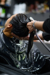 A person receiving hair wash at salon, showing relaxation and care. Water flows over their hair, creating soothing atmosphere.