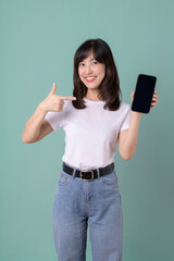 Woman in a white t-shirt pointing at a smartphone with a surprised expression on a green background, highlighting excitement and curiosity.
