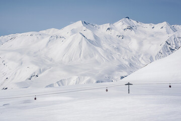 Snowy slopes with gondola to Kobi and ski tracks in nice sunny day. Ski resort Gudauri, Georgia. Caucasus Mountains. Aerial view.