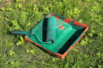 A paint roller in green paint lies in a paint tray on the grass