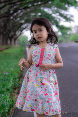 A little girl in a pink floral dress playing outdoors on a sunny day, embodying a carefree childhood.