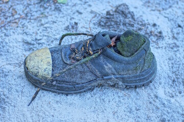 one old dirty leather black boot stands on the gray ground in the street
