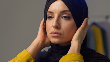 Serious irritated Muslim woman girl wearing hijab in studio adjusting traditional scarf Islamic lady fixing clothes displeased Arabian model sigh strict annoyed gaze female looking at camera portrait