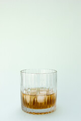 A clear glass with a textured exterior, partially filled with a brown liquid (possibly whiskey or tea). Ice cubes are visible within the liquid, indicating it’s served cold.