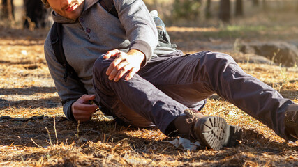 Young upset man having trouble, feeling knee pain during hiking in forest, copy space