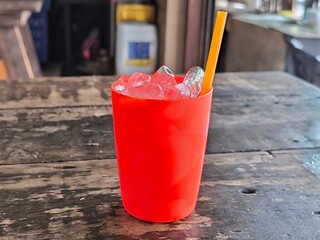 Ice cube in red plastic glass on wooden table. Beverage menu