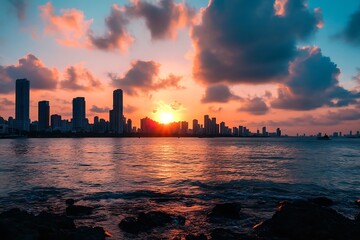 Obraz premium Dramatic sunset cityscape with skyscrapers silhouetted against colorful sky and ocean