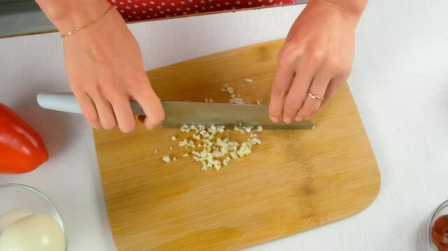 Chef woman cooking skillfully chopping cutting garlic on wooden board, top view. Fresh ingredients, culinary techniques, homemade preparing healthy vegetables, cook food, pungent seasoning for dish.