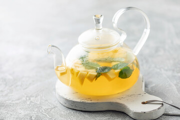 Fruit tea with mango and mint in a glass teapot on the table.