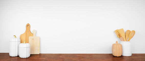 Fall kitchenware, utensils and decor on a wood shelf or counter. Banner against a white wall background with copy space. Autumn kitchen, home cooking concept.