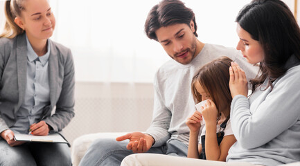 Childhood depression concept. Caring parents comforting their little crying daughter at children psychologist's office