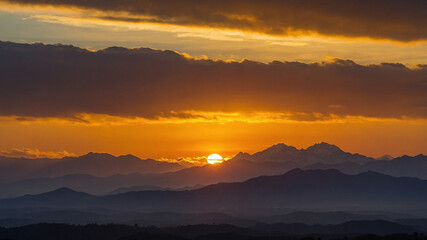 Obraz premium A stunning sunset over a series of lush mountain ranges with mist and golden sky, filling the horizon.