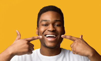 Healthy Teeth, Dental Care Concept. African american man widely smiling and pointing fingers at his...